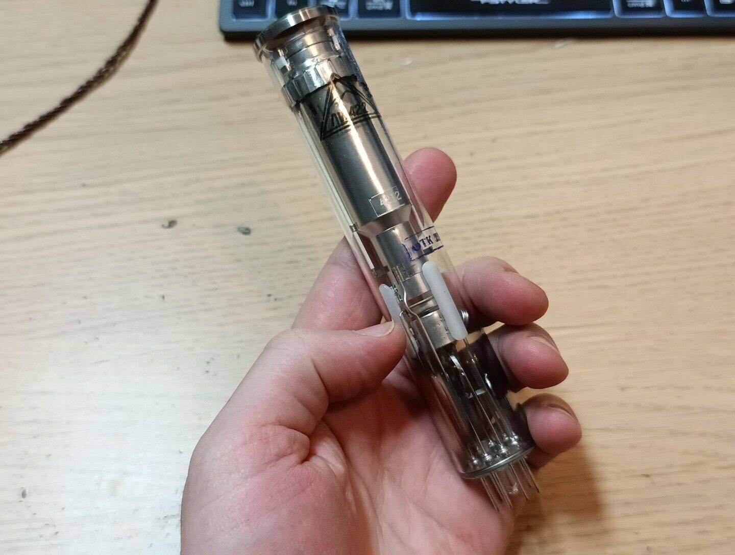 Hand holding a transparent vintage Russian Vidicon tube LI422-2 against a wooden surface with a keyboard in the background.